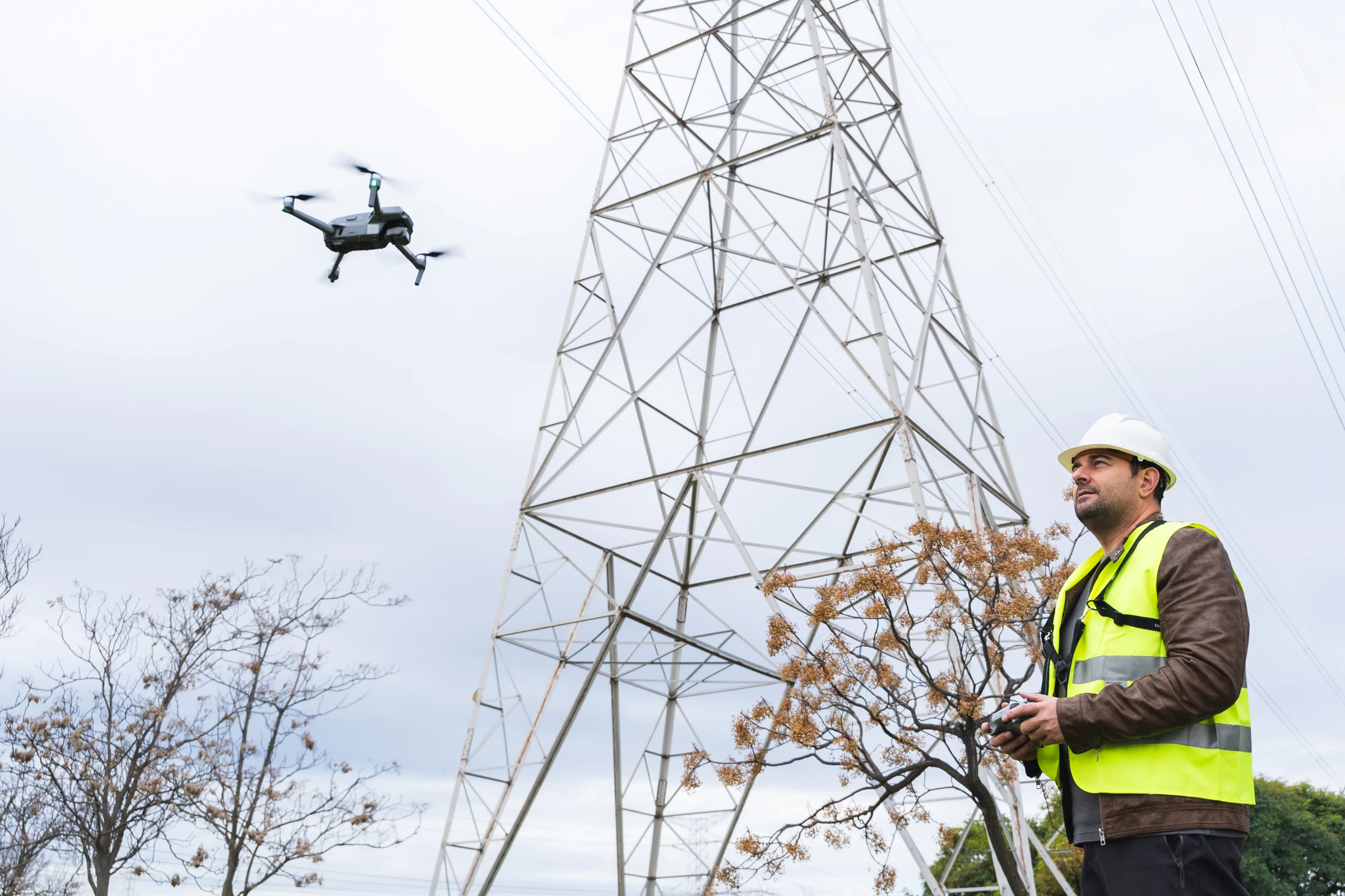 Engineer in a hi-vis vest flying a drone to inspect a high-voltage transmission pylon
